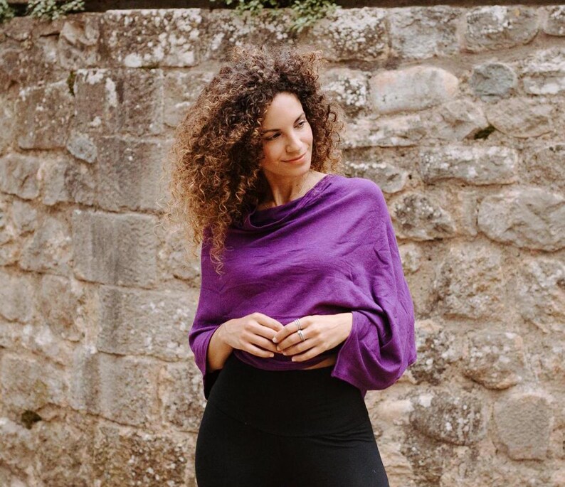 Peut inclure: Une femme portant un haut violet &agrave; col roul&eacute; avec des manches longues et un legging noir. Elle se tient devant un mur en pierre.