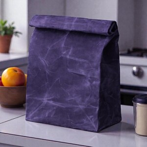 May include: A deep purple, rectangular lunch bag with a roll-top closure. The bag features a distinct, creased, and weathered texture across its surface, giving it a structured yet flexible appearance. It stands upright on a flat surface.