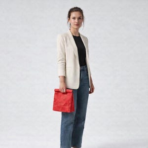 May include: A cream-colored blazer worn over a black top and blue denim jeans, paired with a bright red rectangular handbag. The blazer features a notched lapel and long sleeves, while the jeans have a straight-leg cut and a classic blue wash.