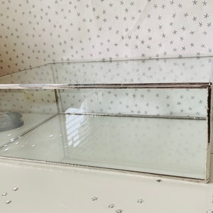 May include: A clear glass display box with a silver metal frame. The box is empty and has a rectangular shape.