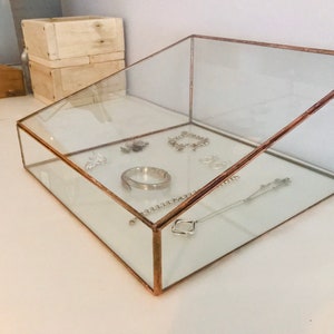 May include: A glass jewellery box with a copper frame. The box is angled and has a variety of silver jewellery inside, including bracelets, necklaces, and rings.