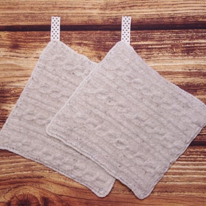 Può includere: Due presine da forno in maglia bianca con nastri bianchi a pois. Le presine sono su una superficie di legno marrone.