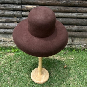 May include: A brown felt hat with a wide brim and a tall crown, displayed on a wooden stand.