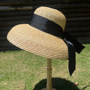 May include: A wide-brimmed straw hat with a black ribbon tied in a bow. The hat is light brown and has a woven texture.
