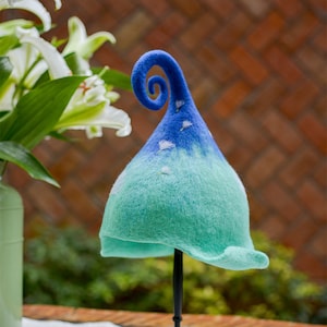 May include: A blue and green felt hat with a curled brim and a whimsical design. The hat is on a black stand.