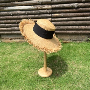 May include: A straw hat with a black ribbon and frayed edges, displayed on a wooden stand against a green grassy background.