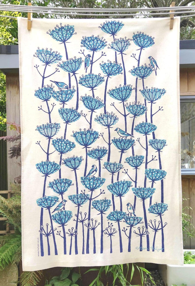Peut inclure: Une serviette de cuisine blanche avec un motif floral bleu et blanc. Les fleurs sont stylis&eacute;es et pr&eacute;sentent un motif g&eacute;om&eacute;trique. De petits oiseaux bleus sont perch&eacute;s sur les fleurs. Le texte "Alison  Hally  Art" est imprim&eacute; dans le coin inf&eacute;rieur droit.