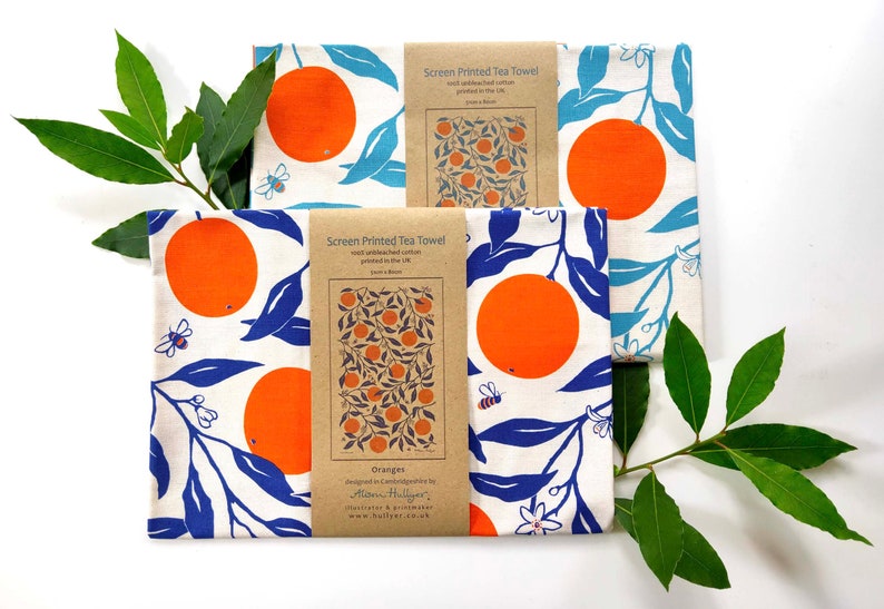 May include: Three tea towels with a white background and a blue and orange orange tree design. The towels are packaged with a brown paper label that says "Screen Printed Tea Towel" and "Oranges".