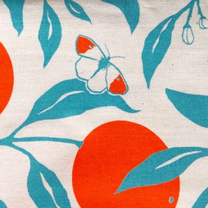 May include: A white fabric with a repeating pattern of orange circles and teal leaves. A white butterfly with orange accents is centred on the fabric.