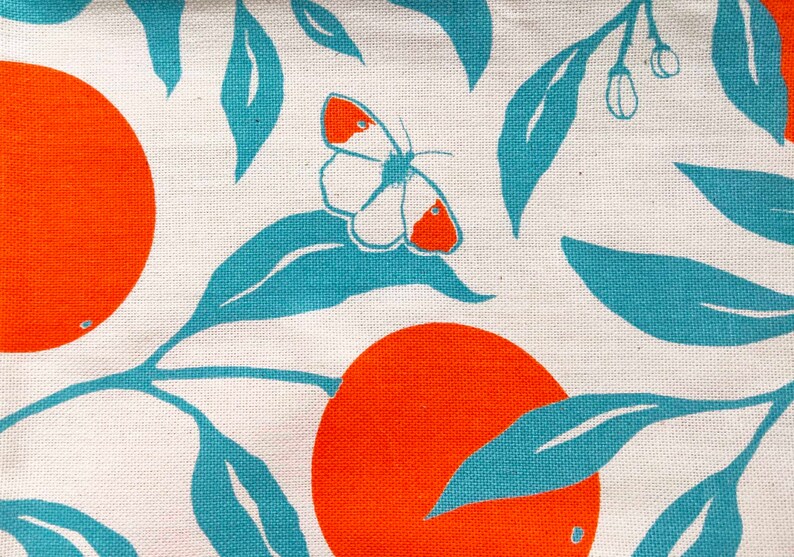 May include: A white fabric with a repeating pattern of orange circles and teal leaves. A white butterfly with orange accents is centred on the fabric.