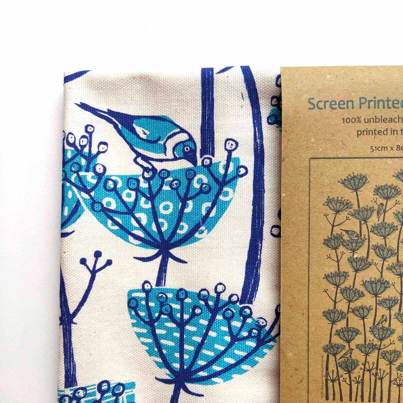 Peut inclure: Une serviette de th&eacute; en coton blanc avec un motif floral bleu et turquoise et un petit oiseau bleu. La serviette de th&eacute; est emball&eacute;e avec une &eacute;tiquette en papier brun qui dit "Screen Printed 100% unbleached printed in the UK 51cm x 80cm".