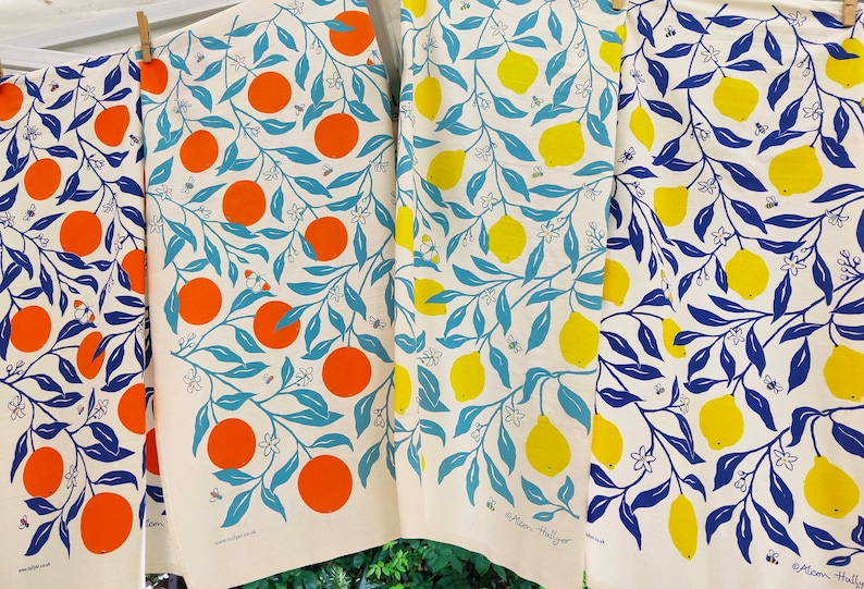 May include: Four tea towels with a white background and a repeating pattern of blue leaves, white flowers, and either orange or yellow citrus fruit. The text "Atom Hullyer" is visible on the bottom right towel.