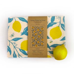 May include: A tea towel with a lemon print. The towel is made of 100% unbleached cotton and is printed in the UK. The towel is 30cm x 30cm. The text on the label reads "Screen Printed Tea Towel 100% unbleached cotton printed in the UK 30cm x 30cm Lemons designed in Cambridgeshire by Alison Hullyer illustrator & printmaker www.hullyer.co.uk"