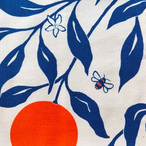 May include: A white fabric with a blue and orange pattern. The pattern features stylised orange slices and leaves, along with a small bee.