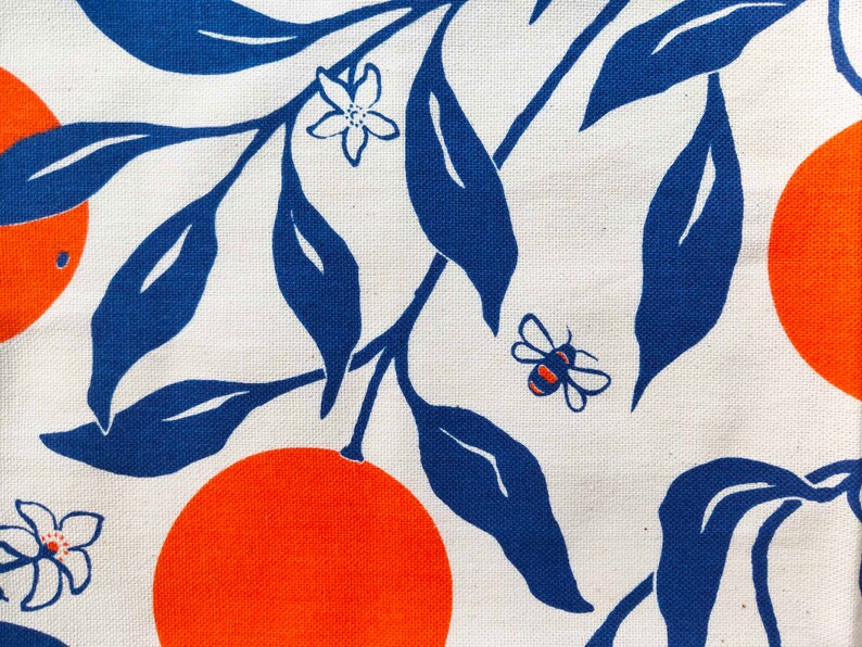 May include: A white fabric with a blue and orange pattern. The pattern features stylised orange slices and leaves, along with a small bee.