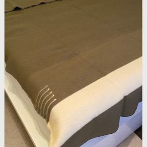 May include: A brown and white striped wool blanket with a subtle texture. The blanket is folded and displayed on a white bed.
