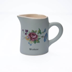 May include: A light blue ceramic creamer with a floral design and the word "Windsor" printed on the bottom.