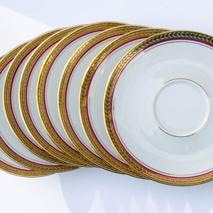 May include: A set of eight white porcelain saucers with gold and burgundy trim. The saucers are stacked in a semi-circle.