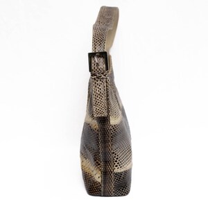 May include: A shoulder bag with a snakeskin pattern in shades of brown, beige, and black. The bag has a single strap with a silver-colored buckle. The bag is made of a textured material.