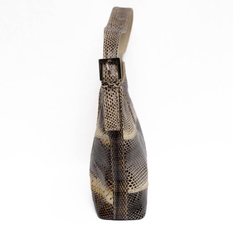 May include: A shoulder bag with a snakeskin pattern in shades of brown, beige, and black. The bag has a single strap with a silver-colored buckle. The bag is made of a textured material.