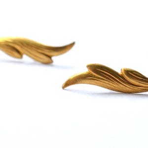 May include: Two gold-colored, leaf-shaped decorative objects. Each object has a curved, flowing design with detailed veining. The objects are positioned on a white background, with one slightly out of focus.