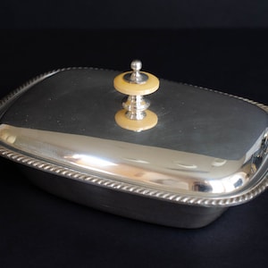 May include: A silver butter dish with a lid and a cream-colored knob. The dish has a rope-like design around the edge.