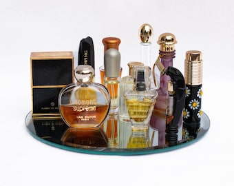 May include: A collection of perfume bottles on a glass tray. The bottles are various sizes and shapes, with some featuring gold accents. The bottles contain a variety of fragrances, including "Moment Supreme" by Jean Patou.