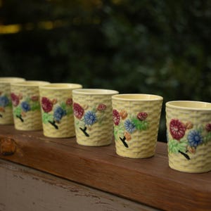 Puede incluir: Seis tazas de cerámica amarilla con diseños florales. Las tazas tienen un patrón tejido y presentan flores en tonos rojos, azules y verdes.