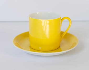 Könnte beinhalten: Ein gelbes Kaffeetassen-Set aus Keramik. Die Tasse hat ein weißes Innenleben und einen abgerundeten Henkel. Die Untertasse ist einfarbig gelb.