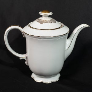 May include: White porcelain teapot with a gold floral design on the lid and gold trim. The teapot has a curved handle and spout, and sits on a scalloped base. The lid is topped with a gold finial.