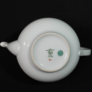 May include: A white porcelain teapot with a rounded body, spout, and handle. The bottom of the teapot features the text "Poesie" and the brand name "Lorenz Hutschenreuther Germany". A green sticker with the number "4" is also visible.