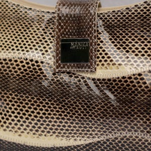 May include: Close-up of a handbag with a snakeskin pattern in shades of brown and beige. The bag features a rectangular flap with the text "MONICA BY MAGLI" on a silver plate. The bag's texture is visible.