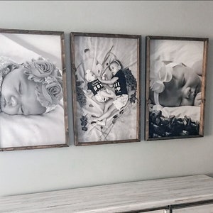 May include: Three black and white framed photographs of babies. The photos are displayed on a white wall above a white dresser.