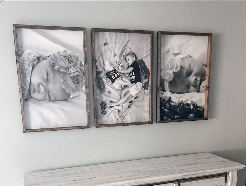 May include: Three black and white framed photographs of babies. The photos are displayed on a white wall above a white dresser.