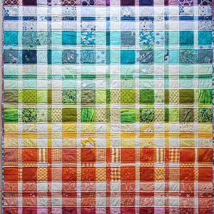 May include: A handmade quilt with a vibrant rainbow plaid design. The quilt features squares of fabric in a spectrum of colors, from purple to red, arranged in horizontal rows. The squares have various patterns and textures, creating a visually appealing textile.