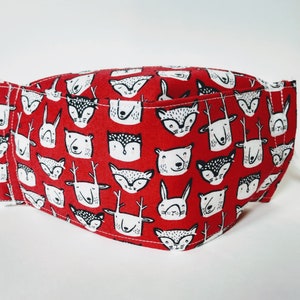 May include: Red fabric face mask with a white and black pattern of various animal faces. The pattern includes deer, foxes, bears, and rabbits.