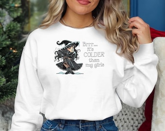 Puede incluir: Sudadera blanca con una ilustración de bruja de dibujos animados y el texto "Brrr... hace más frío que mis chicas".