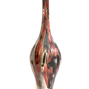 May include: A tall, decorative vase with a slender neck and bulbous body. The vase features a metallic silver base with streaks of red, black, and gold paint. The overall design is abstract and artistic, suitable for home decor.