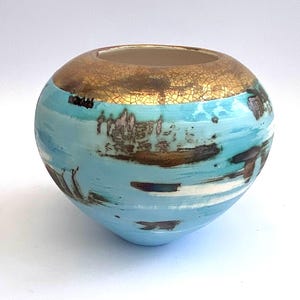May include: A small, round ceramic vase with a blue and white glaze. The top of the vase is decorated with gold leaf.