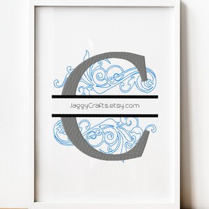 May include: Framed artwork featuring a gray letter "C" with blue floral embroidery. The design is bisected by a black horizontal line, with the text "JaggyCrafts.etsy.com" printed on it. The artwork is in a white frame.