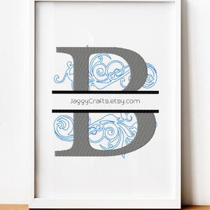 May include: Framed artwork featuring a gray letter "B" with blue floral embroidery. A black horizontal line divides the letter. The text "JaggyCrafts.etsy.com" is displayed. The artwork is in a white frame.