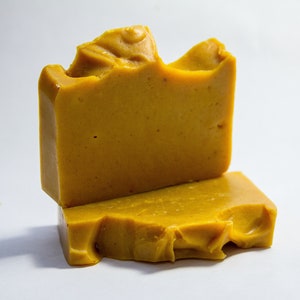 Puede incluir: Dos barras de jab&oacute;n hechas a mano. El jab&oacute;n es de color amarillo dorado con una superficie texturizada. Una barra est&aacute; apilada encima de la otra. La barra superior tiene un borde &uacute;nico e irregular.