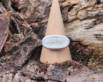 May include: A white oval ring with a silver band and a delicate floral design in gold.