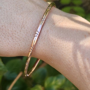 May include: A simple, rose gold bangle bracelet with a textured design. The bracelet is made of metal and has a smooth, polished finish.