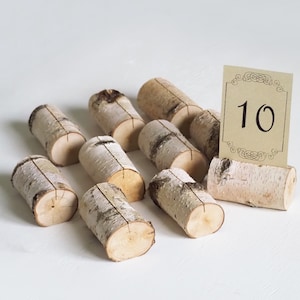 May include: Ten natural birch wood table number holders with a card that says "10" on it. The holders are arranged in a semi-circle on a white surface.