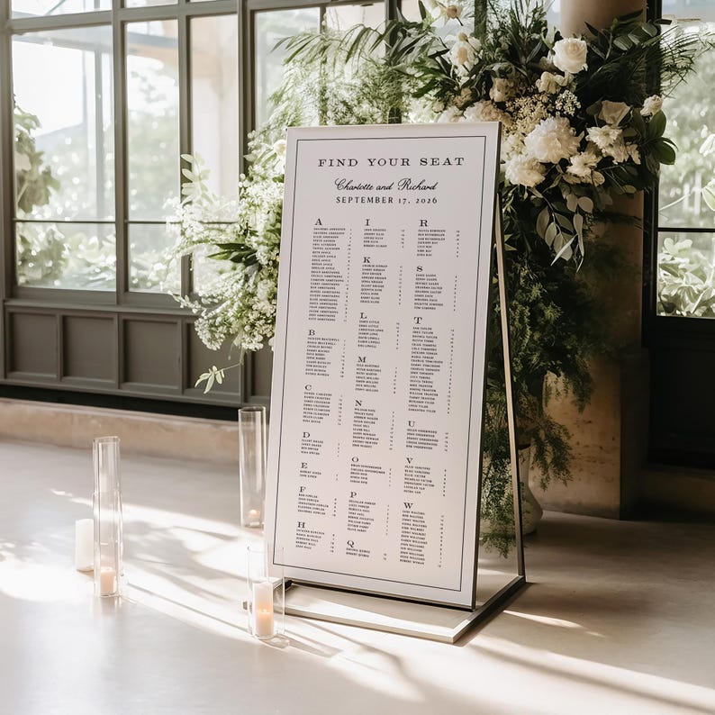 May include: A framed seating chart with the text "Find Your Seat" and the names Charlotte and Richard, dated September 17, 2020. The chart is displayed on a metal stand, with floral arrangements and candles in the background.