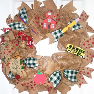 May include: A burlap wreath decorated with red and white polka dot ribbon, black and white checkered ribbon, and school-themed cutouts, including a schoolhouse, a pencil, an apple, and a school bus. The wreath is perfect for a back-to-school theme.