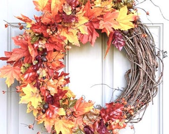 May include: A fall-themed wreath with a grapevine base decorated with red, orange, and yellow maple leaves, berries, and acorns.