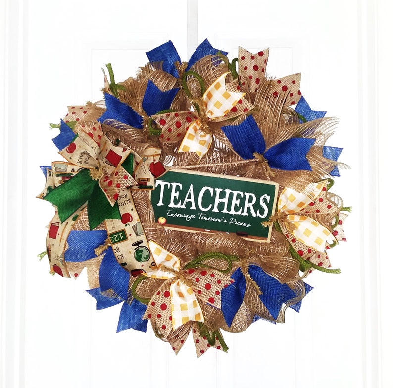 May include: A burlap wreath decorated with blue, yellow, and red ribbon bows. The wreath has a green sign that says "TEACHERS Encourage Tomorrow's Dreams".