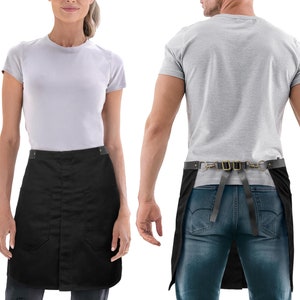 Puede incluir: Delantal negro con una correa de cuero y cierre de hebilla. El delantal tiene dos bolsillos en la parte delantera y un solo bolsillo en la parte posterior.